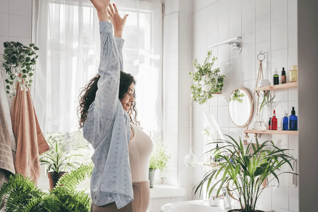A woman stretching in a bright, sunlit bathroom filled with plants, illustrating healthy morning routines and increased energy levels for metabolic health in midlife.