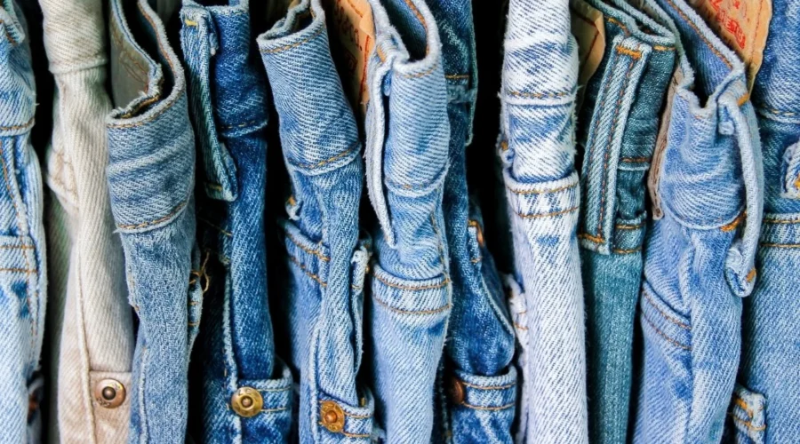 A row of blue denim jeans hanging on a rack, representing the common midlife experience of clothes becoming tight due to hormonal weight shifts and metabolic changes.