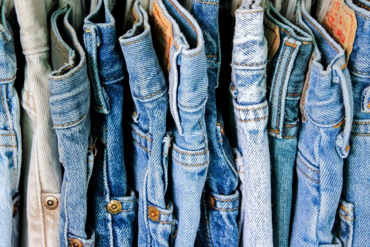 A row of blue denim jeans hanging on a rack, representing the common midlife experience of clothes becoming tight due to hormonal weight shifts and metabolic changes.