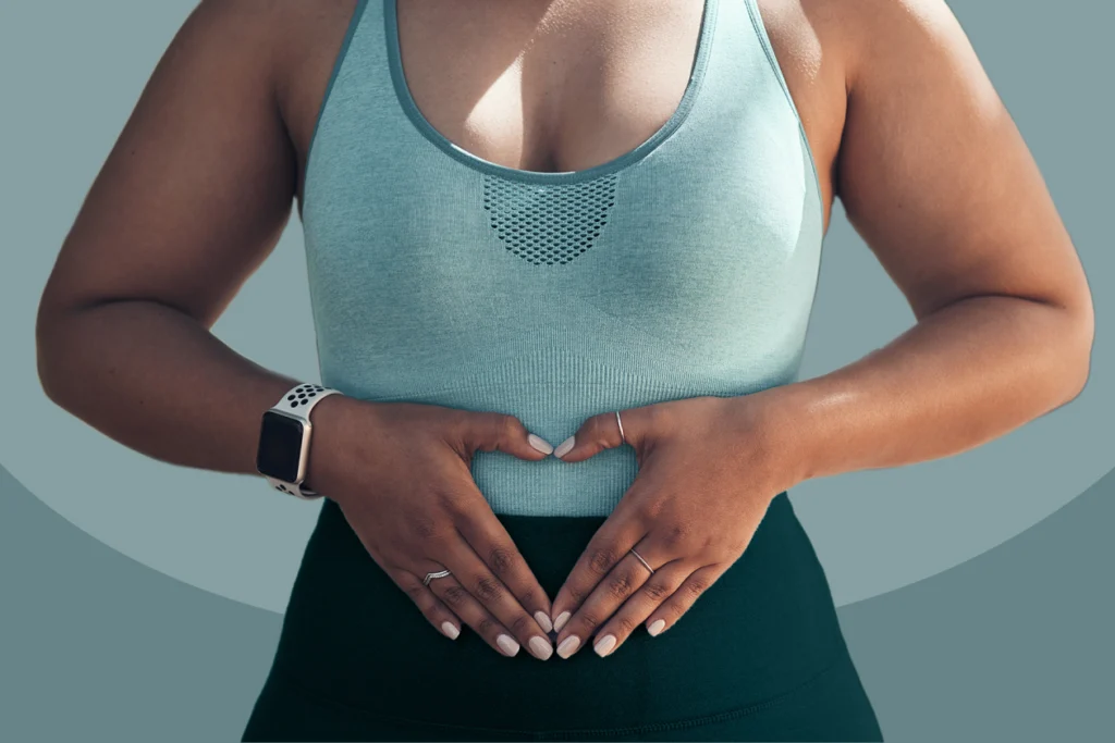 A close-up of a woman in athletic wear making a heart shape with her hands over her stomach, illustrating gut health support and sustainable metabolism.