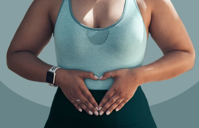 A close-up of a woman in athletic wear making a heart shape with her hands over her stomach, illustrating gut health support and sustainable metabolism.