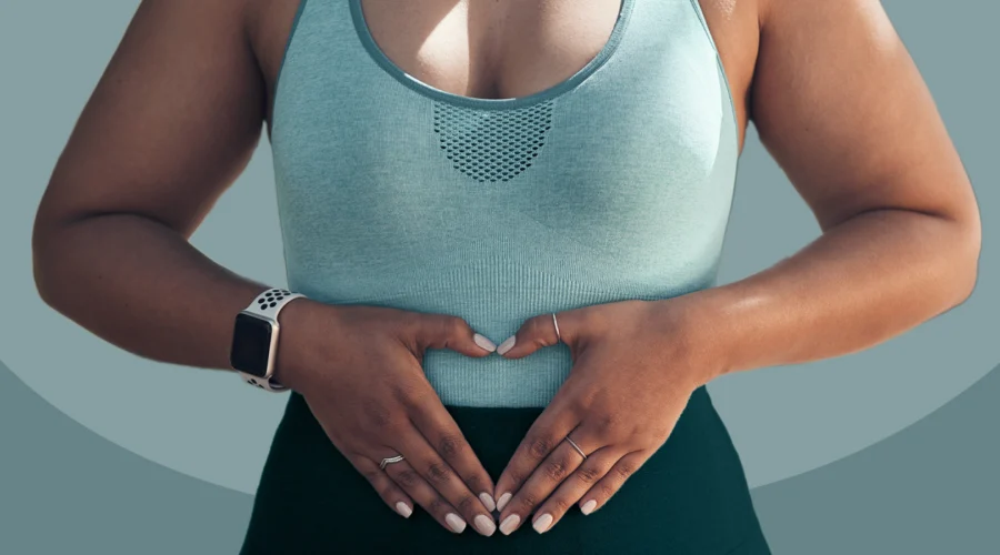 A close-up of a woman in athletic wear making a heart shape with her hands over her stomach, illustrating gut health support and sustainable metabolism.