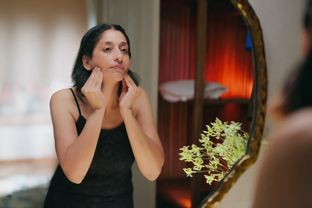 Femme qui examine sa mâchoire et sa peau dans un miroir, un signe courant du visage de la ménopause