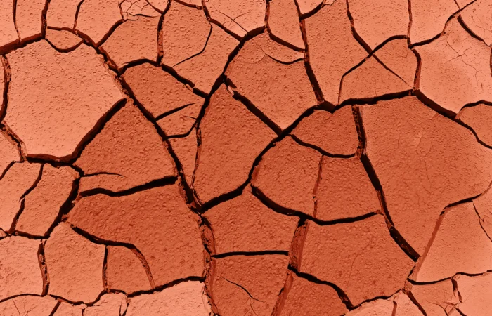menopause-peau-seche-qui-pique Gros plan sur de la terre sèche et craquelée aux tons terracotta, symbolisant la peau sèche et craquelée pendant la ménopause