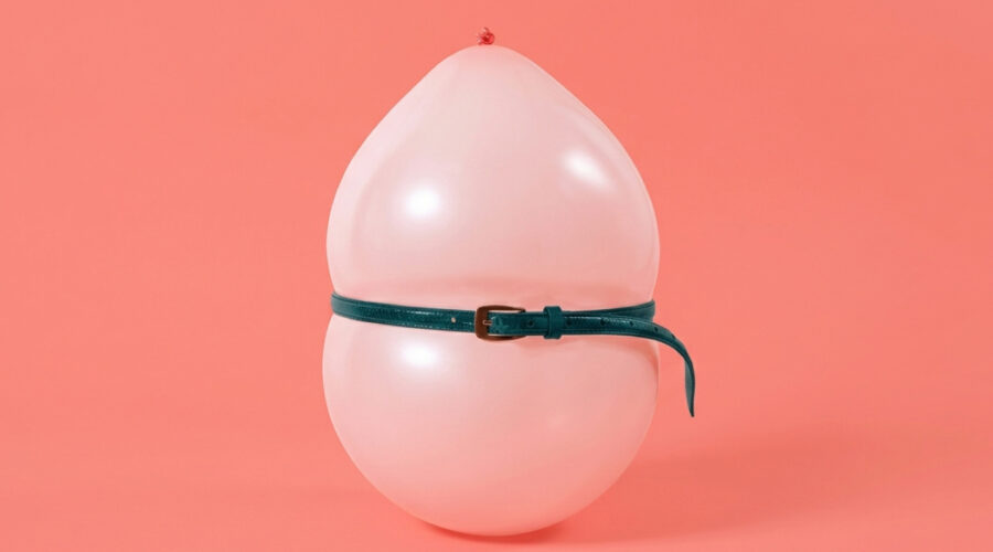 Pink balloon pinched at the middle by a belt, a visual metaphor for menopause bloating