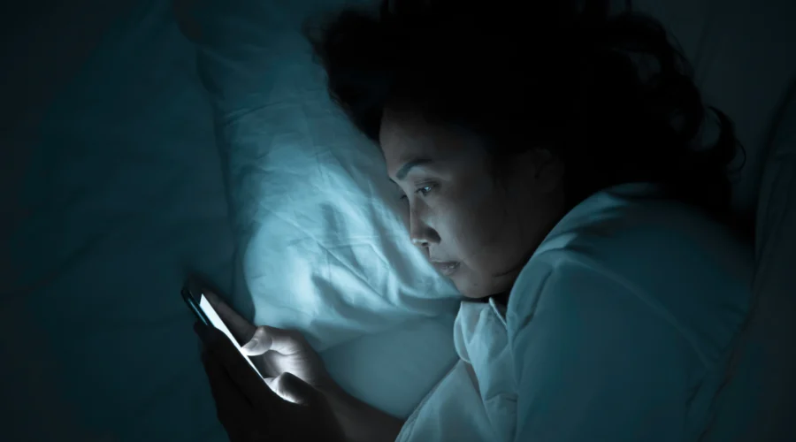 Femme éveillée dans son lit la nuit qui consulte son téléphone pendant une crise d'insomnie en périménopause
