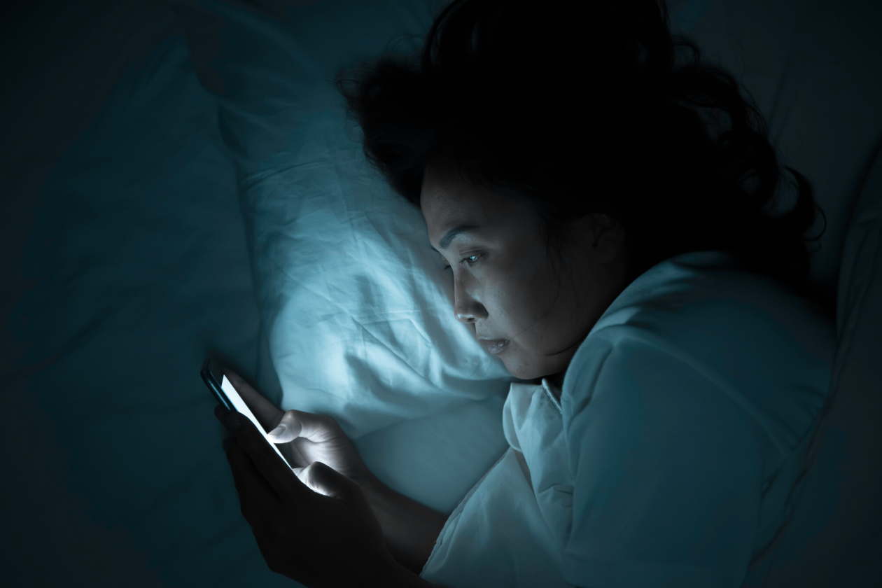 Woman awake in bed at night scrolling her phone during a bout of perimenopause insomnia