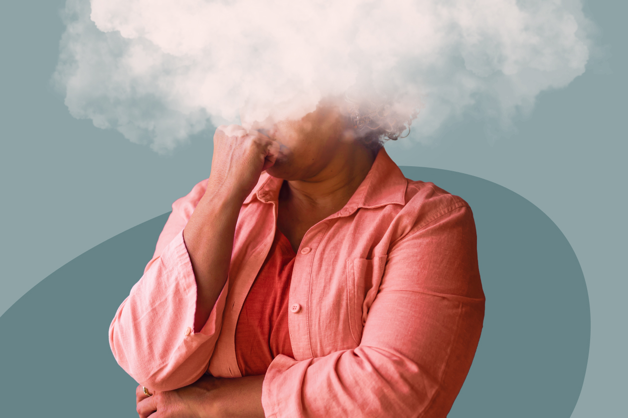 Femme en chemise corail, la main sous le menton et la tête cachée dans un nuage blanc, illustrant le brouillard mental à la ménopause